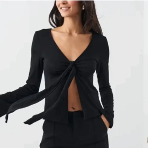 Svart v-ringad topp med knyt - Snygg svart topp med v-ringning och knyt framtill. Toppen har långa ärmar och en stilren design som passar perfekt för olika tillfällen. Använd 1 gång. Slutsåld 💕