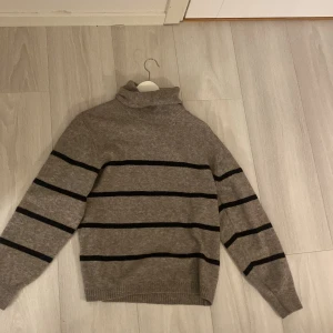 Beige randig polotröja från Lindex - Säljer en mysig beige polotröja från Lindex med svarta ränder. Tröjan har långa ärmar och en klassisk polokrage, perfekt för kyligare dagar. Den är tillverkad i ett mjukt material som håller dig varm och bekväm.