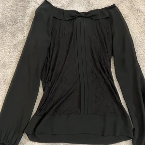 Svart blus från Vero Moda - Elegant svart blus från Vero Moda med långa ärmar och en fin rosettdetalj framtill. Perfekt för en stilren look.