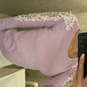 Ljuslila tröja med spetsdetaljer från Newstar - Säljer en ljuslila tröja från Newstar med vackra spetsdetaljer och pärlor längs ärmarna. Tröjan har en rund hals och långa ärmar, perfekt för en stilren look. Passar bra till både jeans och kjol. 🌸OBS! Den är väldigt liten i storleken så den är i storlek Small/S