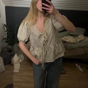 Randig blus med knytning - Säljer en söt randig blus med knytning framtill. Blusen har korta puffärmar och en v-ringad design. Jätte söt till sommarkvällar, skriv för fler bilder om det skulle önskas🥰 (Jag är 175 cm)💓💓