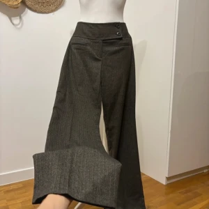 Grå kostymbyxor med knappar - Snygga grå kostymbyxor från Gwen. Byxorna har en vid passform och är perfekta för en elegant look. Tillverkade i ett fint material som ger en lyxig känsla.