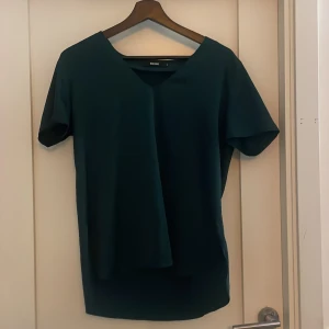 Mörkgrön topp från Bik Bok - Säljer en stilren mörkgrön topp från Bik Bok. Toppen har en v-ringad hals och korta ärmar. Materialet är som silke och väldigt skönt. Använt få gånger så mycket bra skick.