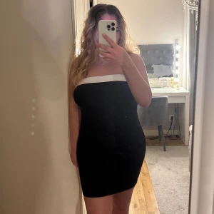 Klänning  - Snygg svart axelbandslös klänning med vit kant upptill 