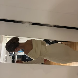 Beige offshoulder långklänning - Elegant beige långklänning med offshoulder-design och tight passform. Klänningen har långa ärmar och en subtil slits som ger en sofistikerad look.  Dubbeltygad för en mer snatched look. 