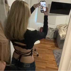 Svart långärmad topp med öppen rygg - Snygg svart långärmad topp med öppen rygg och snörning. Perfekt för en trendig look. Toppen har en ribbad struktur som ger en extra touch.