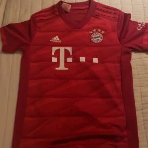 Röd fotbollströja från Adidas - Säljer en röd fotbollströja från Adidas med korta ärmar och klubbmärke på bröstet. Tröjan har vita detaljer och är tillverkad i Climalite-material för optimal komfort. Perfekt för fotbollsfans!