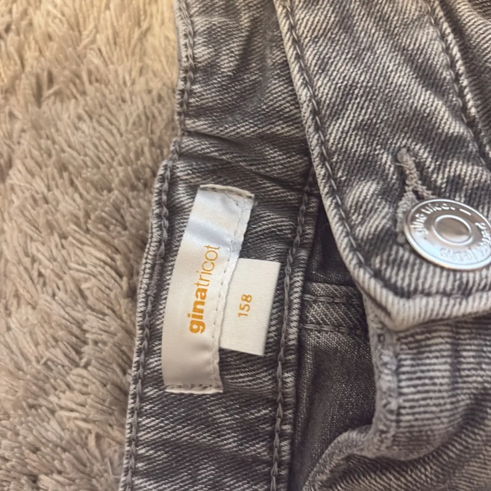 Snygga grå bootcut jeans från Gina Tricot. De har en klassisk femficksdesign och stängs med dragkedja och knapp... Farkut & Housut.