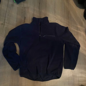 Mörkblå fleece tröja från Everest - Säljer en mörkblå fleece tröja från Everest med halv dragkedja och hög krage. Perfekt för kyliga dagar. Tröjan har en diskret logga på kragen och en praktisk bröstficka med dragkedja.