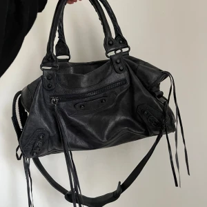  axelväska / handväska - Snygg svart axelväska i skinn med coola detaljer och dragkedja. Väskan har långa remmar och flera fack för praktisk förvaring. Perfekt för att ge din outfit en edgy touch.