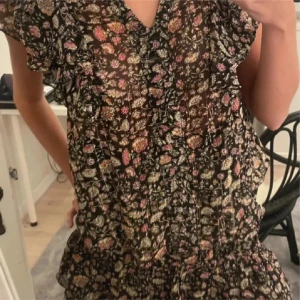 Blommig klänning med snörning - Charmig blommig klänning med korta ärmar och v-ringning. Den har en fin snörning i ryggen och volangdetaljer som ger en romantisk touch. Perfekt för sommarens varma dagar. (Lånade bilder, kontakta för egna!)