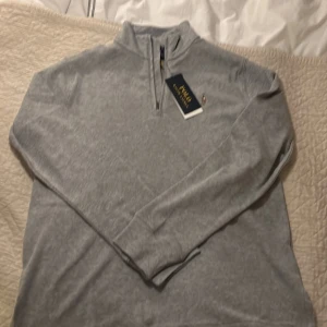 Grå tröja från Polo Ralph Lauren - Säljer en stilren grå tröja från Polo Ralph Lauren. Tröjan har en dragkedja vid halsen och långa ärmar. Perfekt för en avslappnad och snygg look.Nypris 1500 Den är helt oanvänt säljer pga för liten storlek plastbox finns också.hör av dig för frågor och funderingar.Priset kan diskuteras vid snabb affär!