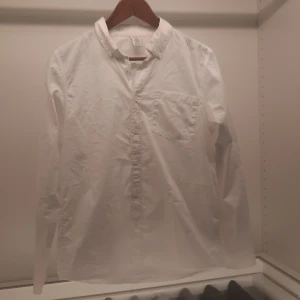 Vit skjorta från Lindex - Säljer en klassisk vit skjorta från Lindex i storlek 170. Skjortan har en bröstficka och knappar framtill. Perfekt för en stilren look.