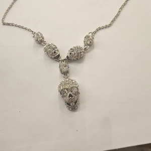 Silverfärgat halsband med dödskallar Rock by Sweden  - Unikt silverfärgat halsband med tre glittriga dödskallar. Kedjan är tunn och elegant, vilket gör att de detaljerade dödskallarna verkligen står ut. Perfekt för att ge en edgy touch till din stil.