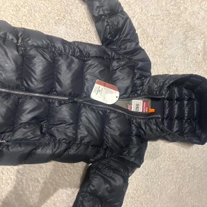 BARN STORLEK M(Xs i vanlig storlek) Svart dunjacka från Parajumpers barn storlek.  - Säljer en snygg svart dunjacka från Parajumpers. Jackan har en quiltad design med dragkedja framtill och en praktisk huva. Perfekt för kyliga dagar och håller dig varm och stilren. Märkesdetaljer på ärmen ger en extra touch. Köpte den för 4500 och säljer den för 1900kr
