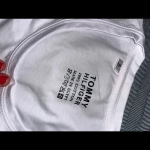 Vit t-shirt från Tommy Hilfiger - Säljer en klassisk vit t-shirt från Tommy Hilfiger i 100% bomull. T-shirten har en liten broderad logga på bröstet och är kortärmad. Perfekt för en stilren look.