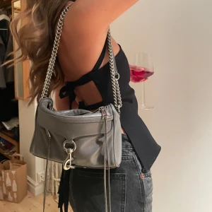 Rebecca minkoff väska - Så fin grå axelväska i skinn från Rebecca minkoff, cool kedjerem och dragkedja. Väskan har en stilren design med en dekorativ metallspänne framtill. Perfekt för att ge din outfit en edgy touch.