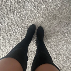 Svarta overknee boots - Snygga svarta overknee boots med mellan hög klack och rundad tå. Perfekta för att ge en stilren look till din outfit. De är gjorda i ett mjukt material som ger en bekväm passform.