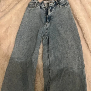 Tre par jeans till salu - Första paret är ljusblå jeans med hög midja och rak passform. Andra paret är beige cargopants med flera fickor och loose fit. Tredje paret är ljusblå jeans med normal passform och midwaist.
