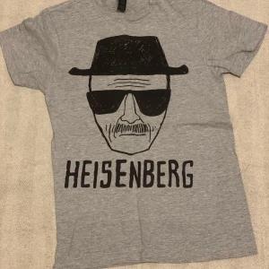 Grå t-shirt med Heisenberg-tryck från Gildan - Säljer en grå t-shirt från Gildan med ett coolt Heisenberg-tryck i svart. T-shirten är kortärmad och gjord i mjuk bomull. Perfekt för fans av kultserien Breaking Bad 🖤