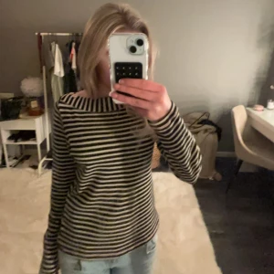 Randig långärmad tröja - Säljer en stilren randig tröja med långa ärmar. Tröjan har en klassisk svart och vit färgkombination med små rosa detaljknappae vid axeln och är perfekt för en avslappnad look. Den är tillverkad i ett mjukt material som gör den bekväm att bära hela dagen.🩷🩷