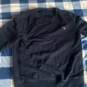 Gant tröja - Säljer en stilren mörkblå tröja från GANT med rund hals och diskret logga på bröstet. Tröjan har långa ärmar och ribbade muddar vid ärmslut och nederkant. Perfekt för en avslappnad look.  Bor i Kalmar