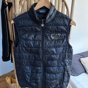 Svart dunväst från Emporio Armani - Snygg svart dunväst från Emporio Armani i storlek S säljes. Skanna QR-koden för autenticiteten på västen. 