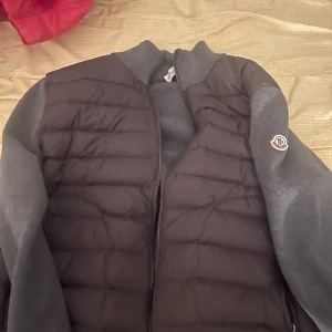 Grå moncler cardigan - Snygg svart och grå jacka från Moncler, storlek L, skulle rekommendera för någon som är lite mindre i storleken då cardigans är små i storlekar, liten defekt är att ena sidan av lappen är lös men inte svårt att fixa och inget som syns utåt därav det låga priset. Pris går att diskuteras.