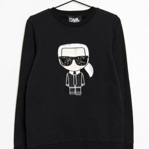 Svart tröja med tryck från Karl Lagerfeld - Snygg svart tröja från Karl Lagerfeld med ett coolt tryck av en figur med solglasögon på framsidan. Tröjan har långa ärmar och en rund halsringning. Perfekt för en stilren look.