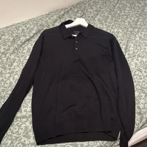 Svart tröja från Massimo Dutti - Snygg svart tröja från Massimo Dutti i mjuk material. Tröjan har långa ärmar och en klassisk krage med knappar. Perfekt för en stilren look.