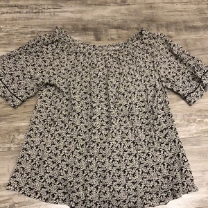 Svartvit blommig blus - Säljer en söt svartvit blommig blus med korta ärmar. Blusen har ett fint blommönster och en bekväm passform. Perfekt för en avslappnad stil.