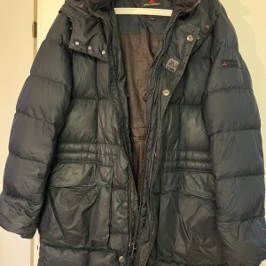 Svart dunjacka från Peuterey - Säljer en svart dunjacka från Peuterey med lång ärm och dragkedja. Jackan har en quiltad design och en hög krage för extra värme. Perfekt för kalla dagar.