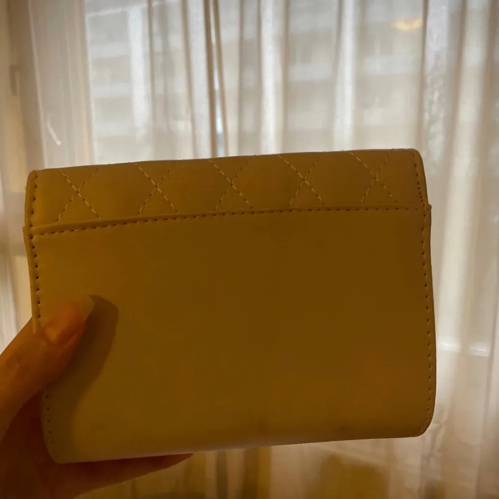 Säljer en beige handväska med quiltat mönster och en elegant gulddetalj på framsidan. Väskan har en praktisk dragkedja inuti för säker förvaring. Perfekt för att ge din outfit en chic touch. Finns något märke på baksidan men syns inte så mycket. . Laukut & Käsilaukut.