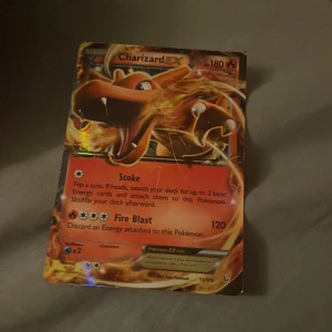 Charizard EX Pokémonkort - Säljer ett Charizard EX Pokémonkort med 180 HP. Kortet har en glansig yta och visar Charizard omgiven av eld. Det har attacker som 'Stoke' och 'Fire Blast'. Perfekt för samlare eller spelare som vill stärka sin kortlek.