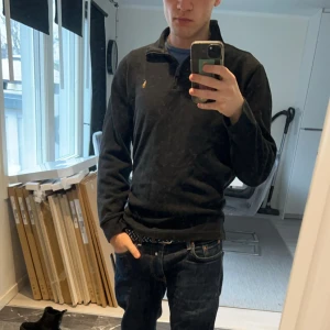 Half zip Ralph Lauren tröja - Säljer en stilren svart tröja från Ralph Lauren med en liten dragkedja vid halsen. Tröjan har långa ärmar och en diskret logga på bröstet. Perfekt för en avslappnad och snygg look.