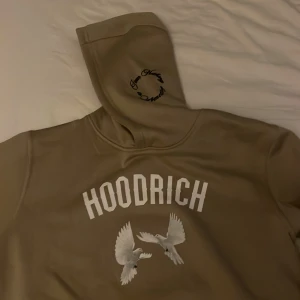 Beige hoodie från Hoodrich - Säljer en beige hoodie från Hoodrich med tryck av vita duvor och texten 'From Nothing to Something'. På framsidan står 'Always Proud Never Satisfied'. Perfekt för en avslappnad stil.