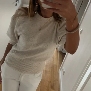 Beige stickad tröja - Säljer en stilren beige stickad tröja med korta ärmar. Tröjan har en ribbad kant vid ärmslut och nederkant, vilket ger en snygg passform. Perfekt för en avslappnad och trendig look.