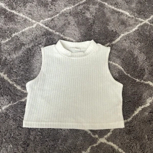 Vit ribbad ärmlös topp från SHEIN - Säljer en stilren vit ribbad topp från shein. Den är ärmlös med en hög krage och har en croppad passform. Perfekt för lager-på-lager eller sommarens varma dagar.