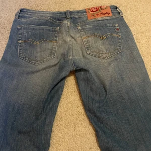 Blå jeans från Replay - Snygga blå lågmidjade jeans från Replay med klassisk femficksdesign och en lätt tvättad look. De har en normal passform och är perfekta för en avslappnad stil. Märkeslogga på baksidan ger en extra touch.