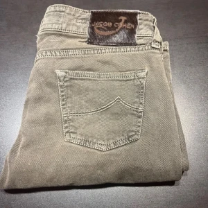 Grå byxor från Jacob Cohen - Snygga grå byxor från Jacob Cohen med klassisk design. Byxorna har en normal passform och är tillverkade i ett mjukt bomullsmaterial. De har en stilren look med knappar och en liten ficka fram. Perfekta för en stilren vardagslook. Size 29