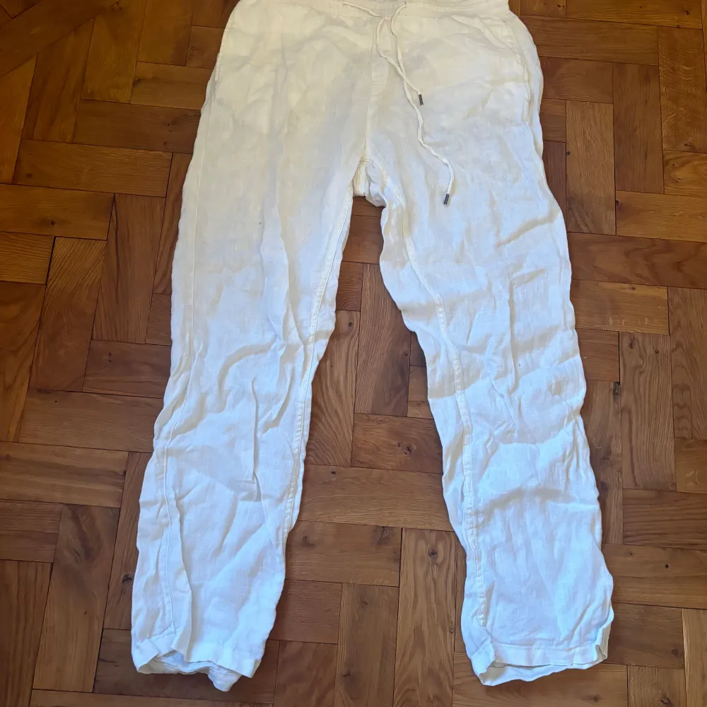 Snygga vita linnebyxor från East West med avslappnad passform och snörning i midjan. Perfekta för varma dagar med sitt lätta och luftiga material. Byxorna har en enkel design med fickor på sidorna.. Farkut & Housut.