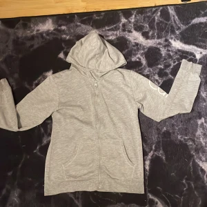 Grå hoodie från Calvin Klein - Säljer en stilren grå hoodie från Calvin Klein med dragkedja framtill. Tröjan har långa ärmar och en luva, samt Calvin Klein-logga på armen