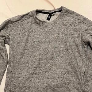Grå tröja från Adidas - Säljer en snygg och bekväm grå tröja från Adidas. Perfekt för både träning och vardag. Tröjan har en normal passform och är tillverkad i mjukt material som känns skönt mot huden. Den är långärmad och har en enkel design som passar till det mesta. Perfekt för höst och vår!säljs för 60