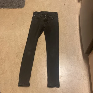 Svarta jeans från Nudie Jeans - Säljer ett par svarta slim jeans från Nudie Jeans i storlek 28/30. De är i bra skick och har en klassisk femficksdesign med knappgylf. Perfekta för både vardag och fest! Säljer för dem va för små/tighta för mig.