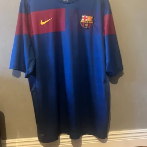 Blå och röd FC Barcelona fotbollströja - Säljer en snygg FC Barcelona fotbollströja från Nike. Den är blå med röda detaljer och har klubbens emblem på bröstet. Tröjan är kortärmad och perfekt för alla Barca-fans. Passar både för match och vardag!