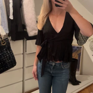 Svart omlottopp med knytband - Säljer en snygg svart omlottopp med knytband i midjan. Knappt använd och i jättebra skick. Perfekt för både vardag och fest! 🖤