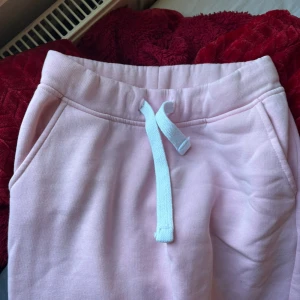 Rosa mjukisbyxor i storlek XS - Säljer ett par supermysiga rosa mjukisbyxor i storlek XS. De har en bekväm resårmidja med snörning och praktiska fickor. Perfekta för en chill dag hemma eller en snabb tur till affären. Det finns en liten fläck på benet, men annars i bra skick.