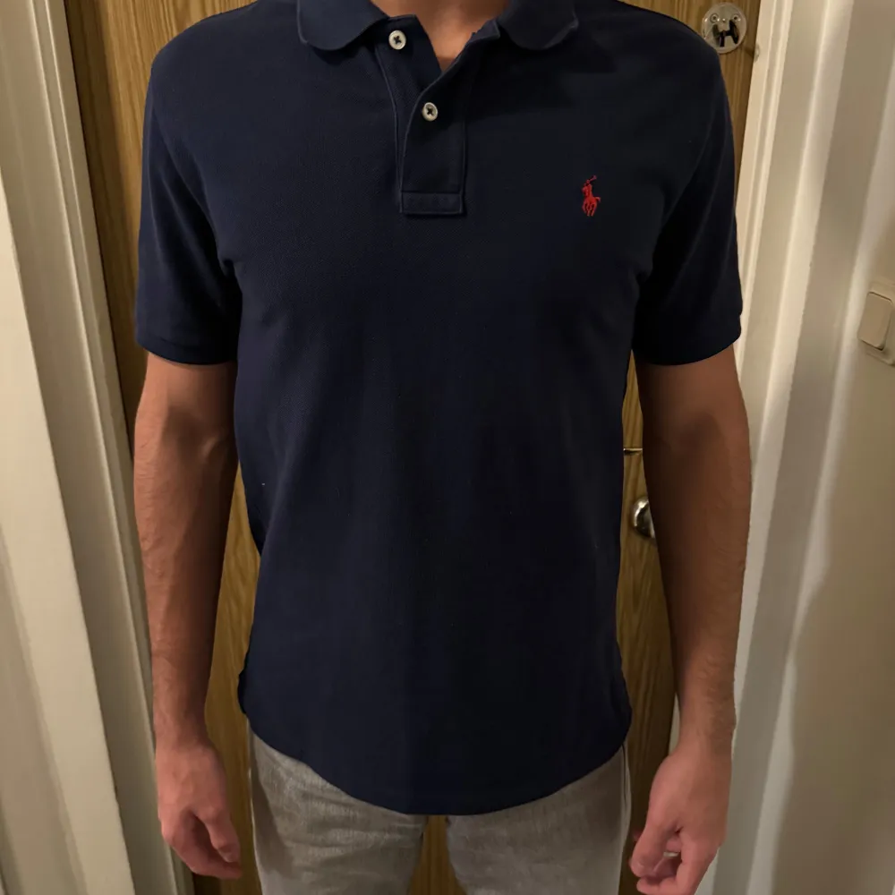 Säljer en snygg mörkblå pikétröja från Ralph Lauren. Den har en klassisk krage med två knappar och det ikoniska röda broderade logotypen på bröstet. Perfekt för både vardag och fest! Tröjan är i bra skick och passar till det mesta. Skicka ett meddelande vid intresse! Nypris 1400kr                . T-shirts.