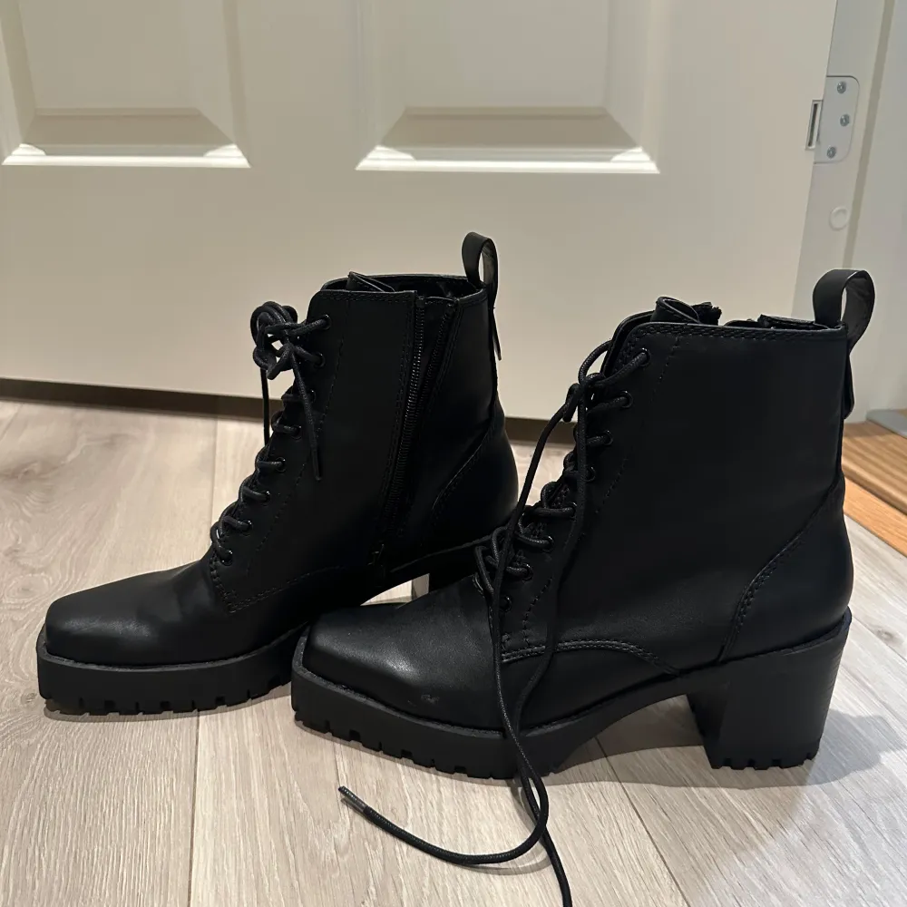 Snygga svarta boots med snörning och dragkedja på sidan. De har en robust klack och en grov sula som ger bra grepp. Perfekta för höst och vinter, dessa boots är både stiliga och praktiska. Passar till både vardag och fest!. Skor.