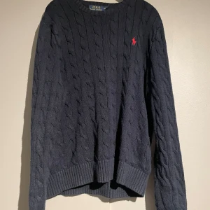 Mörkblå stickad tröja från Polo Ralph Lauren - Säljer en snygg mörkblå stickad tröja från Polo Ralph Lauren. Den har ett klassiskt flätmönster. Perfekt för kyliga dagar med sina långa ärmar och ribbade kanter. Passar både till vardags och lite finare tillfällen. Tar också emot byten.   Skick 7/10